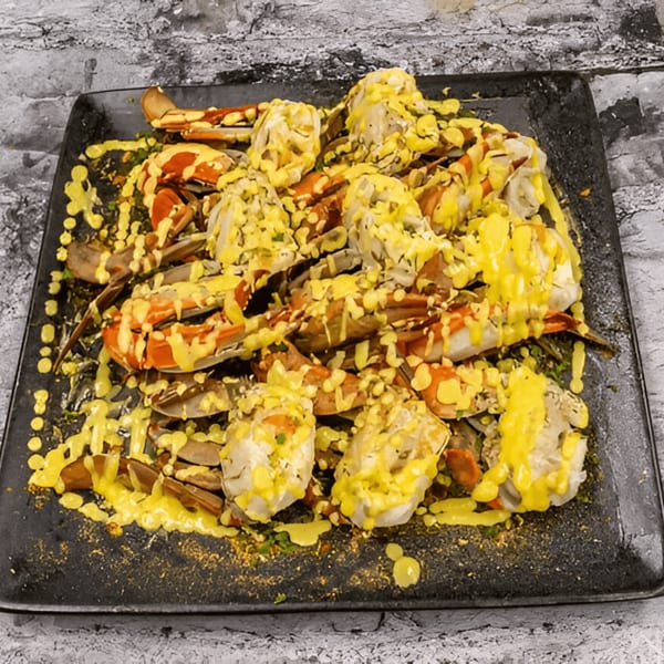 G'Ville Seafood N' Chicken's blue crabs and shrimp covered in yellow sauce on a black platter.