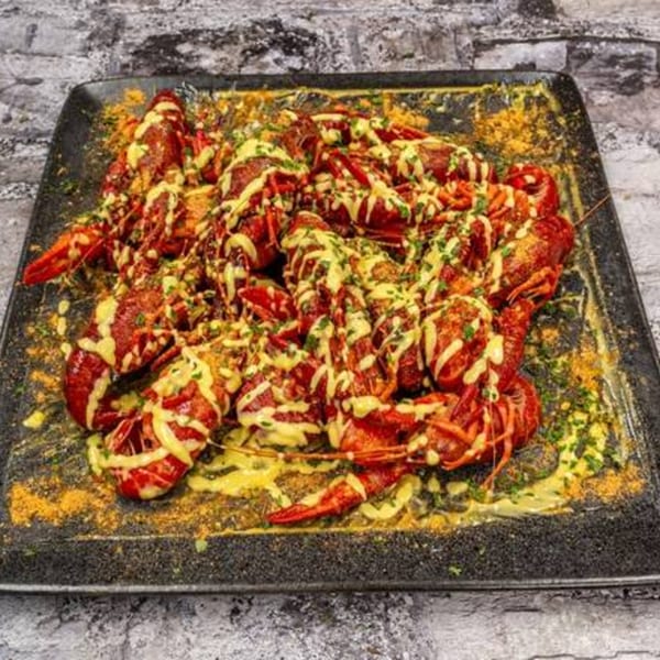 A platter of G'Ville Seafood N' Chicken's red crawfish, drizzled with yellow sauce and green herbs.
